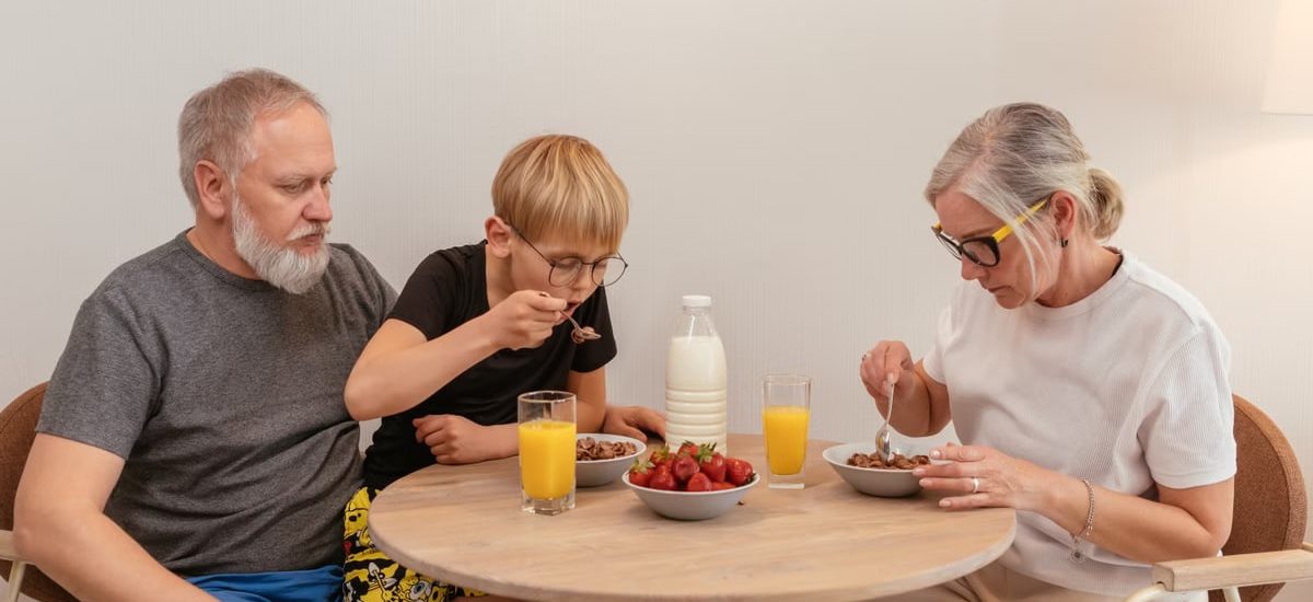A family of three enjoying breakfast around a wooden table at home.