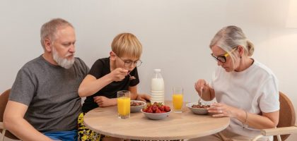 A family of three enjoying breakfast around a wooden table at home.