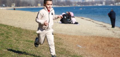 Young boy in a tracksuit runs energetically by the waterfront, embodying the joy of a sunny day outdoors.