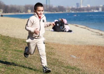 Young boy in a tracksuit runs energetically by the waterfront, embodying the joy of a sunny day outdoors.